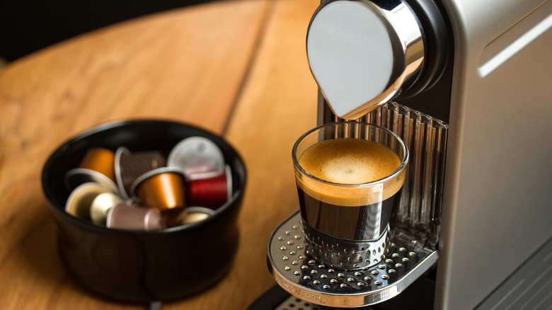 Nespresso machine brewing fresh coffee with bowl of Nespresso pods next to it