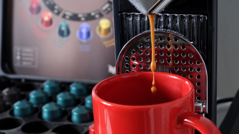 Nespresso machine pouring coffee into a red mug, blue capsules in background