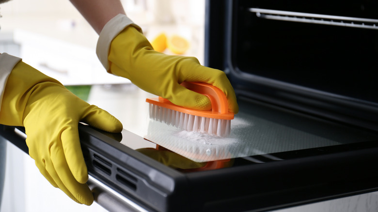 Person wearing gloves cleaning oven door with baking soda and a scrub brush