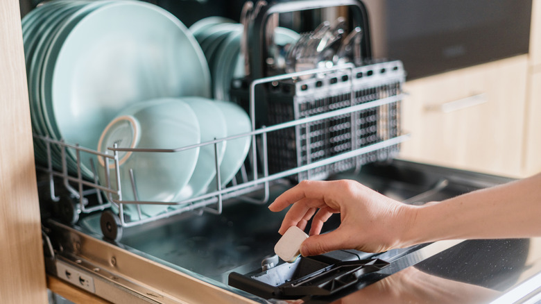 Person adding detergent tablet to dishwasher