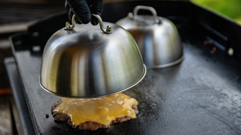 placing a cheese melting dome over a grilling hamburger