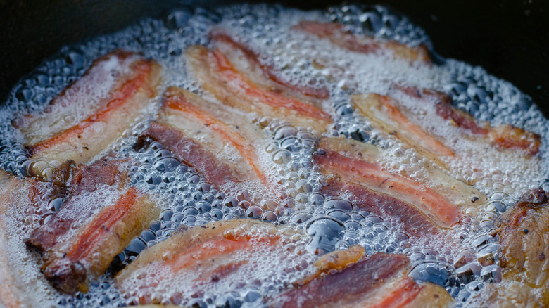 Bacon slices cooking in bubbling grease