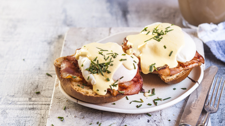 Eggs Benedict on a white plate with fork and knife