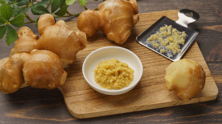 ginger root and grated ginger in small bowl on wood cutting board