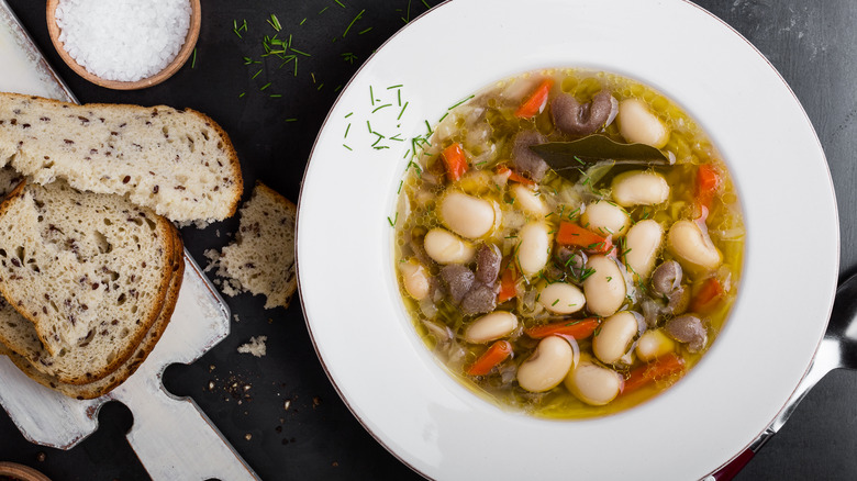 white bean and mushroom soup in white bowl with side of seeded bread