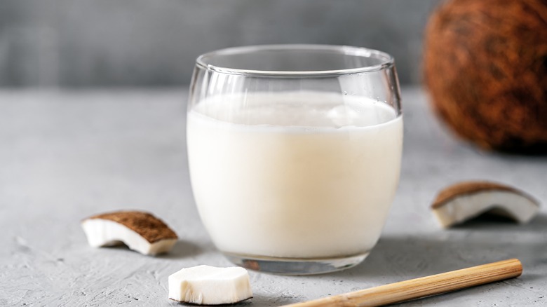 glass of coconut milk with coocnut pieces on grey background