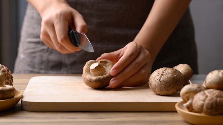 hands cutting shiitake mushrooms on wood cutting board