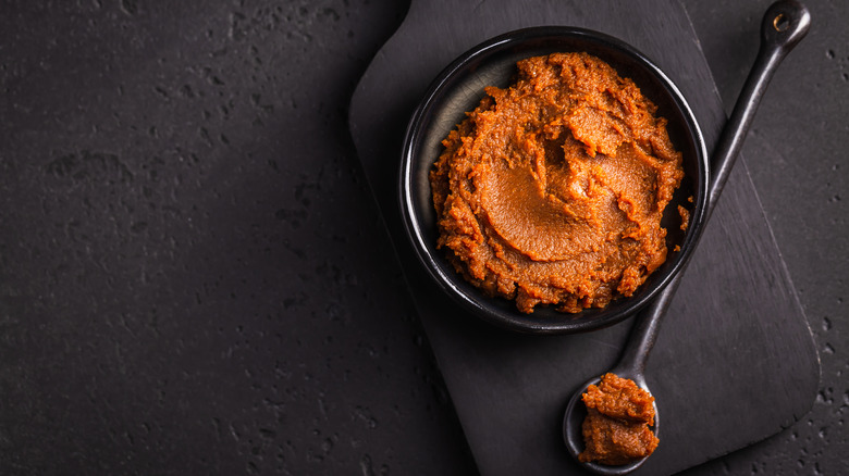 bowl and spoon of red miso paste on black background