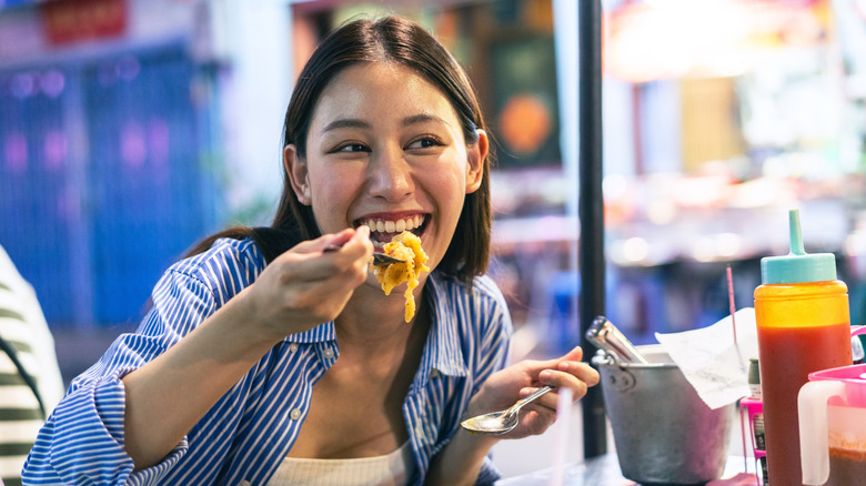 Smiling woman eating noodles with fork