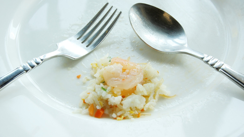 Fork and spoon in an almost empty white bowl of fried rice