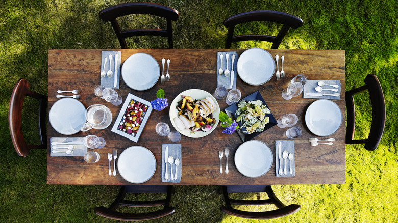 Overhead shot of wooden dining table on grass with six place settings