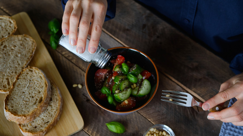 Hand shaking salt over bowl of vegetables on brown table