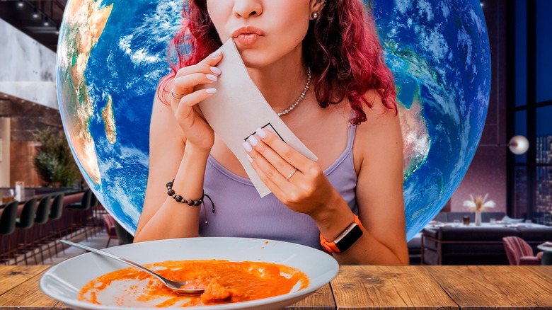 Woman cleaning mouth with white napkin behind empty plate of food, in front of world globe