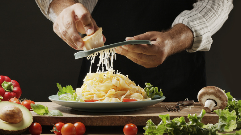 chef hands grating cheese onto pasta