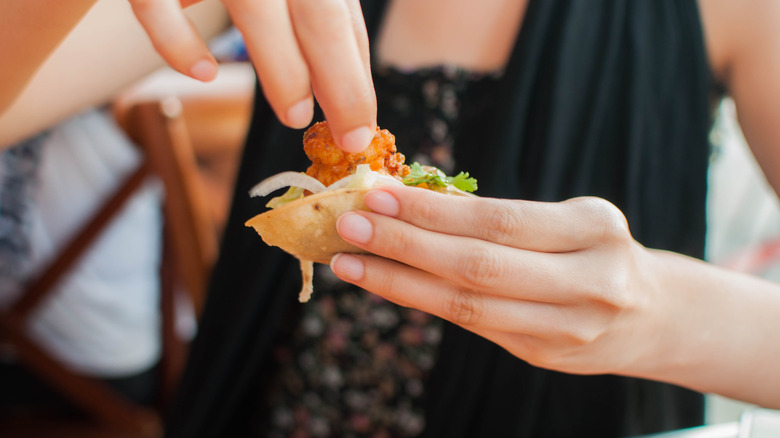 Two hands holding small taco with shrimp