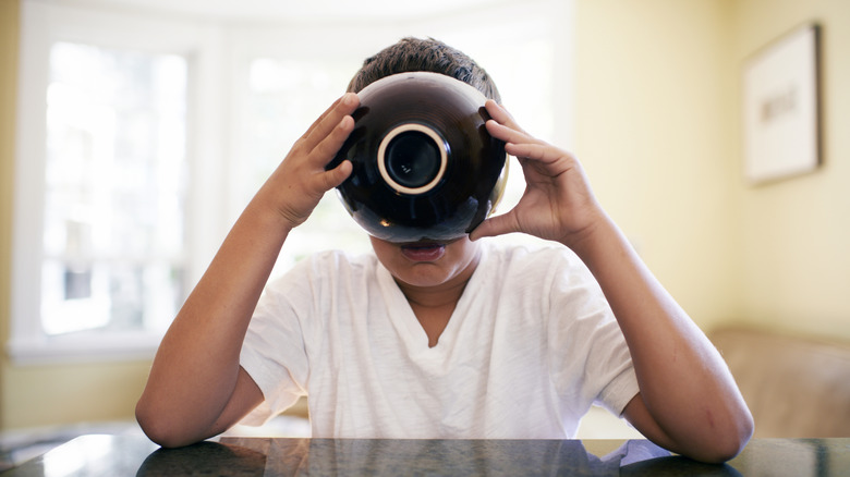 Person with elbows on table holding black bowl up to their mouth, drinking