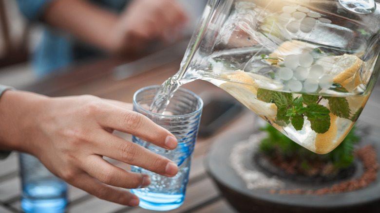 Pouring drink from pitcher into glass held in hand