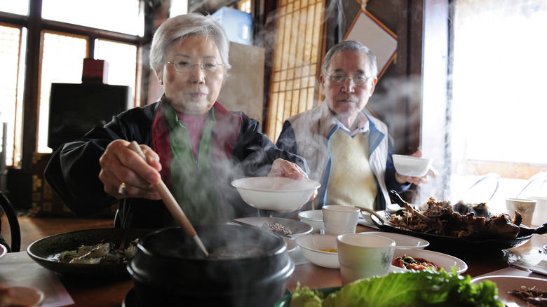 Elderly Asian man and woman serving food into white bowls