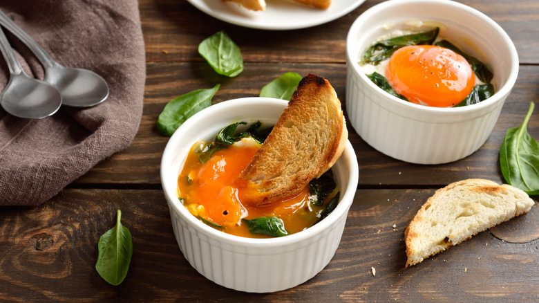 White ramekin of eggs and greens with bread dipped in it