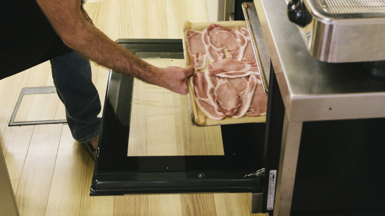 Someone placing a baking tray of bacon in an open oven