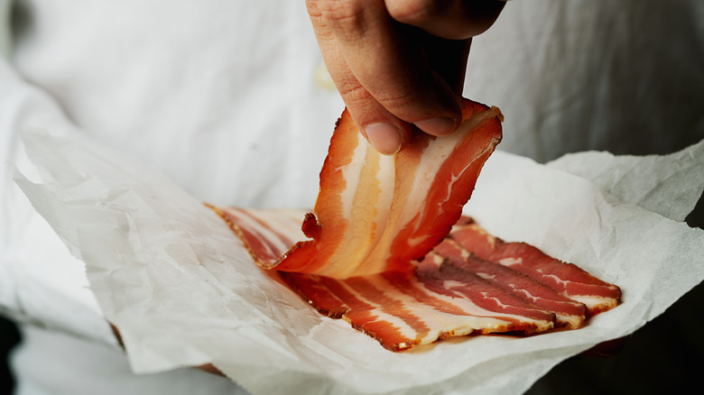 Hand pulling a piece of thin sliced bacon from a pack