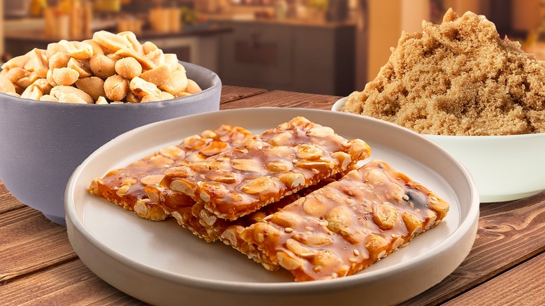 Plate of peanut brittle surrounded by bowls of ingredients on a wooden tabletop