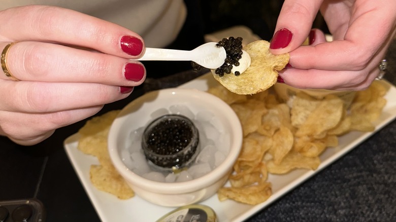 Putting a spoonful of caviar on top of creme fraiche and potato chips