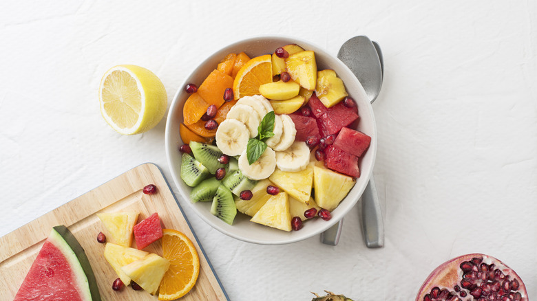 A bowl and chopping board with cut mixed fruit