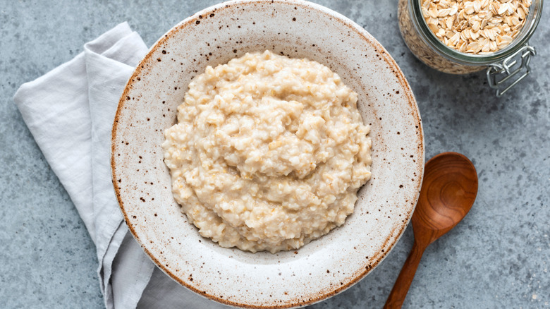 A bowl of plain oatmeal with a napkin, wooden spoon, and dry oats