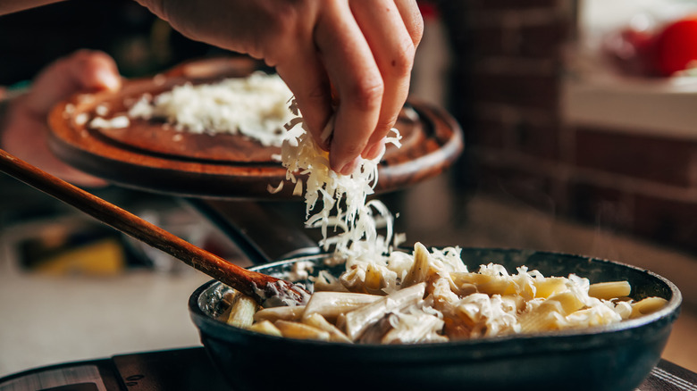 Hand sprinkling Parmesan on pasta