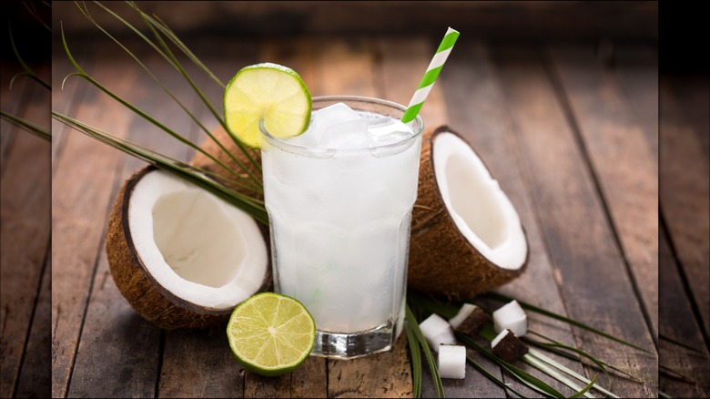 Glass of coconut water with coconuts opened on the side