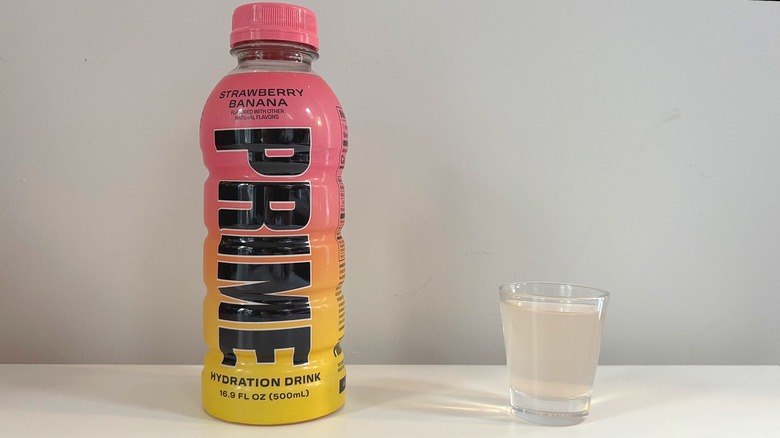 Prime Strawberry Banana bottle next to shot glass with drink on white table