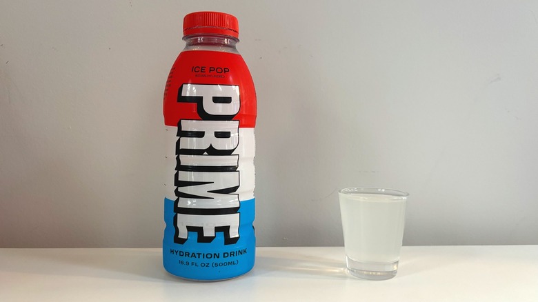 Prime Ice Pop bottle next to shot glass with drink on white table