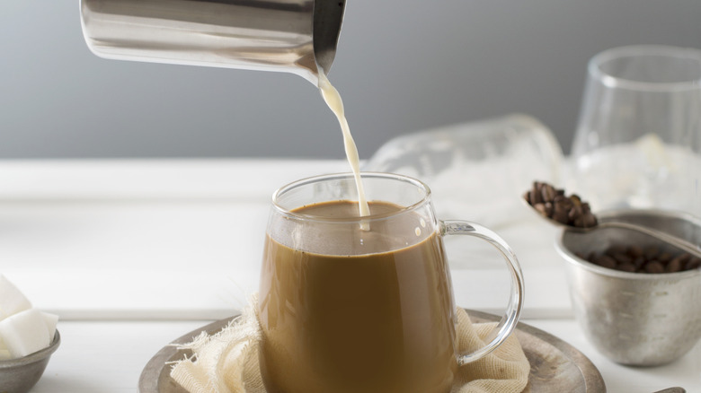 Milk being poured into tea in a clear mug