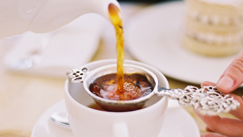 Tea being poured from tea pot into a cup through a decorative tea strainer