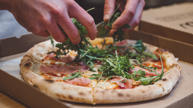 Hands spreading arugula on pizza