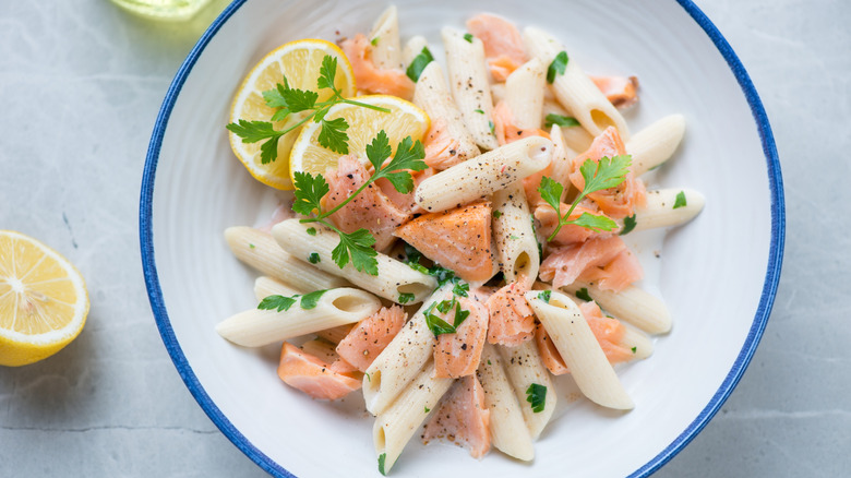 Bowl of cream salmon pasta with parsley and lemon wedges