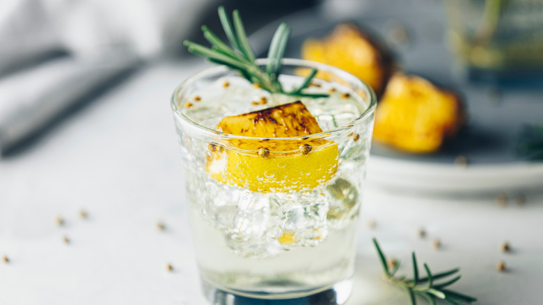 Cocktail glass filled with ice and clear liquid and garnished with charred lemon and rosemary