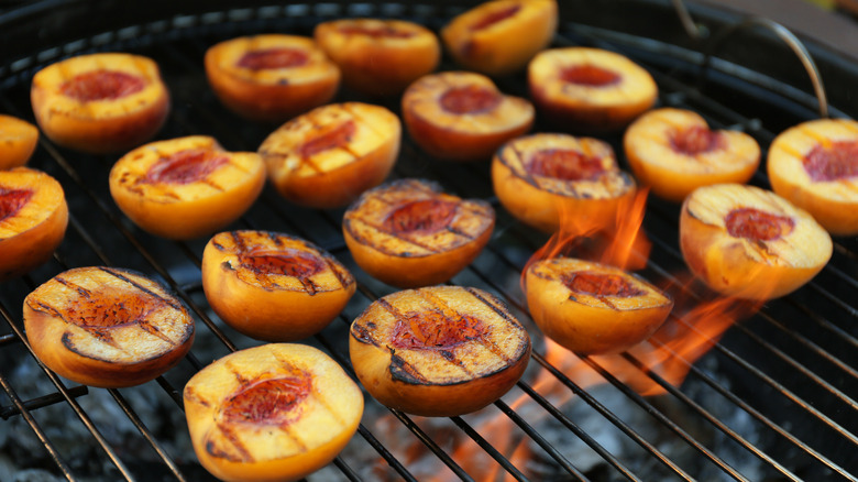 Ripe peaches cut in half charring on the grill over open fire