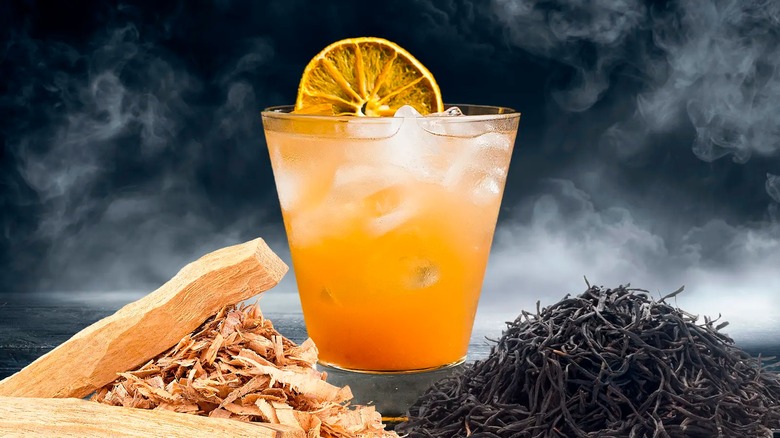 Wood chips and loose black tea with a cocktail and charred fruit slice