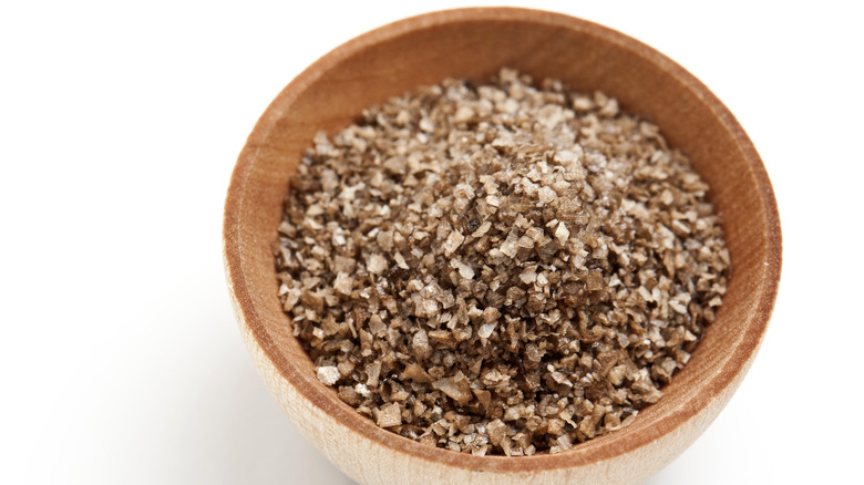 Brown smoked salt in a wooden bowl with a white background