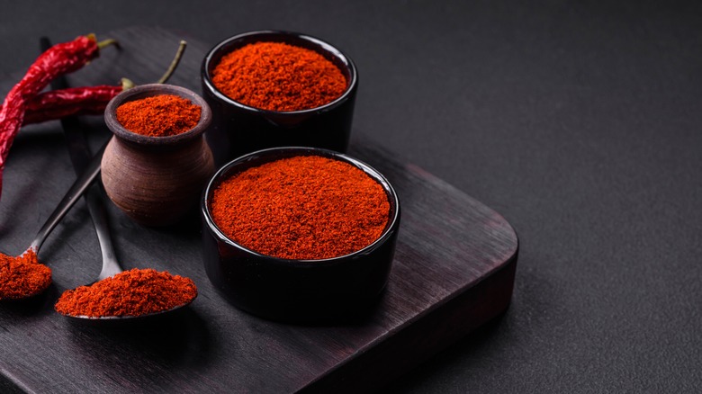 Smoked red paprika packed in several bowls on a black background, with whole dry peppers in the back