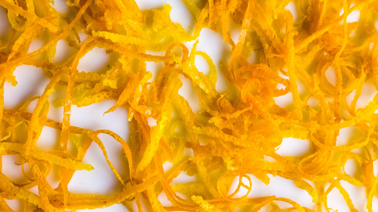 Fresh orange zest on a white plate. Raw citrus zest, grated orange peel, fresh zest on a white background.