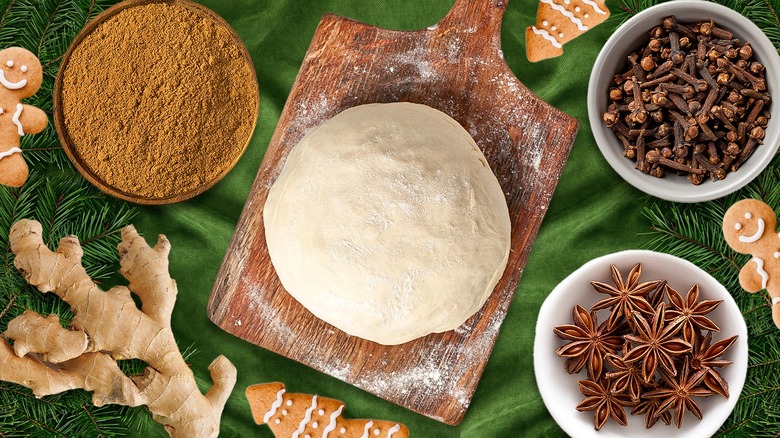 a ball of dough on wooden cutting board with spices around it and gingerbread men