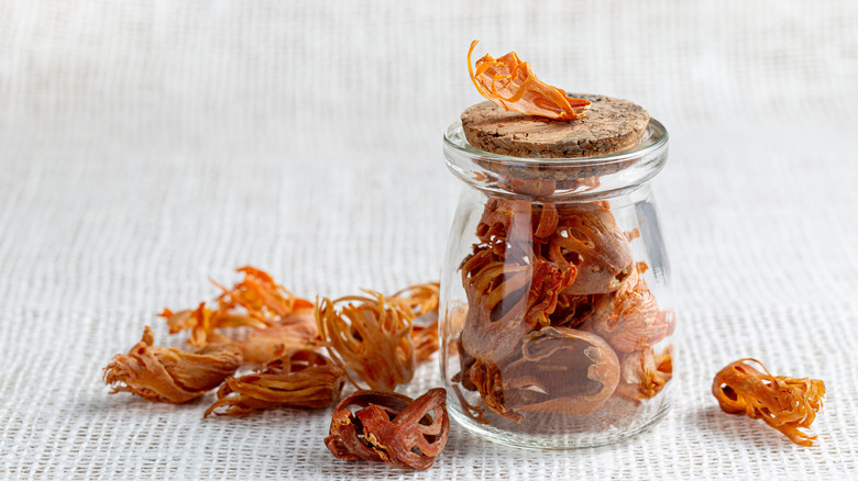 Nutmeg mace spice in glass jar with wooden topper, pile of mace on white woven fabric