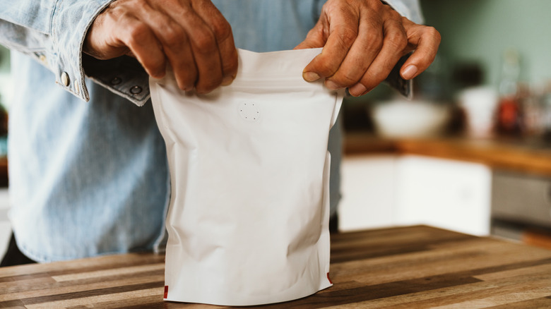 A closeup view shows hands closing a bag of coffee beans.