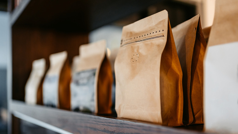 Brown bags of coffee beans sit on a wooden shelf.