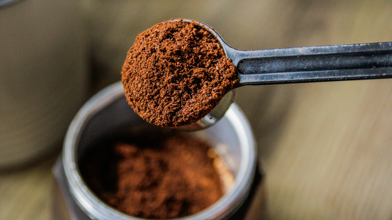 A metal scoop is filled with ground coffee.