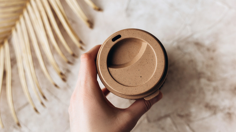 A hand is holding a compostable coffee cup.