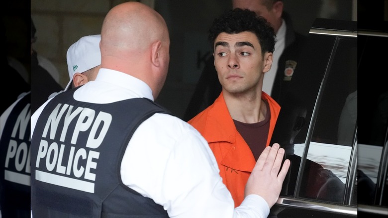 Luigi Mangione in orange jumpsuit and NYPD officer next to car